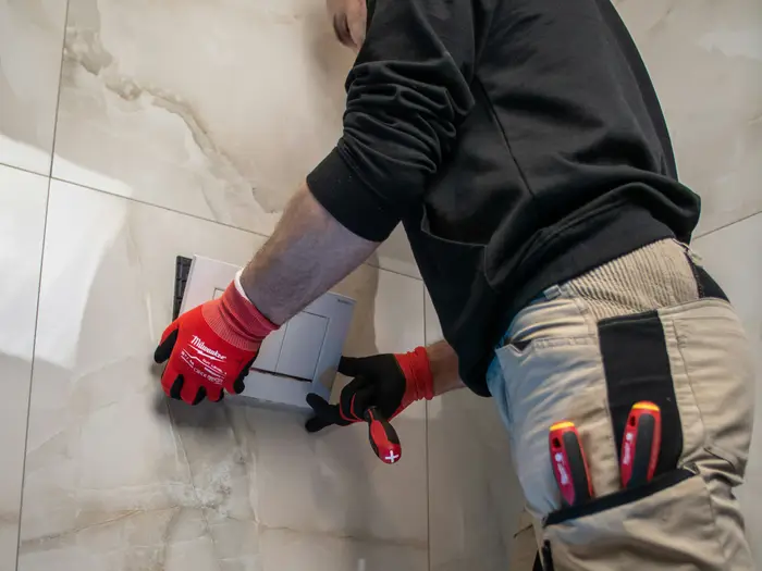 Vakman in werkkleding met handschoenen aan het werk aan een betegelde wand