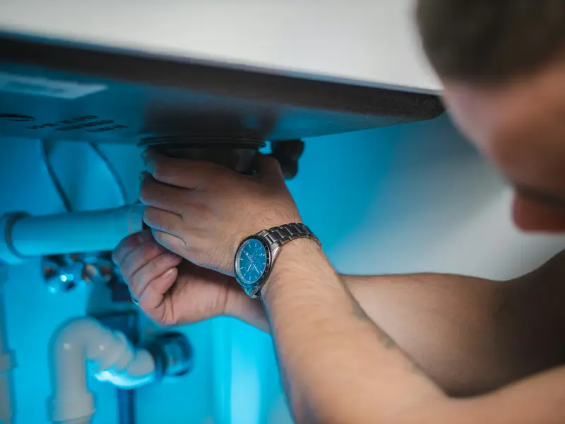 Loodgieter werkt onder een wastafel aan de sifon en afvoer